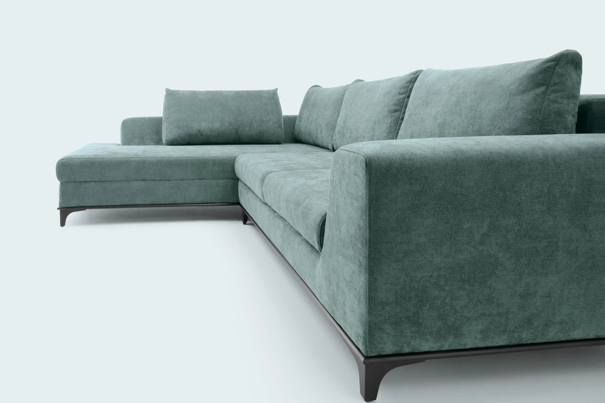 A modern L-shaped sectional sofa upholstered in textured sage green fabric, featuring dark wooden legs, photographed against a clean, light gray studio background.