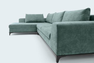 A modern L-shaped sectional sofa upholstered in textured sage green fabric, featuring dark wooden legs, photographed against a clean, light gray studio background.