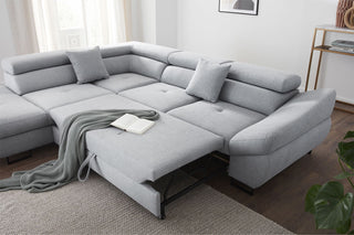 Gray sectional sofa in a living room setting with a blanket and book on it.