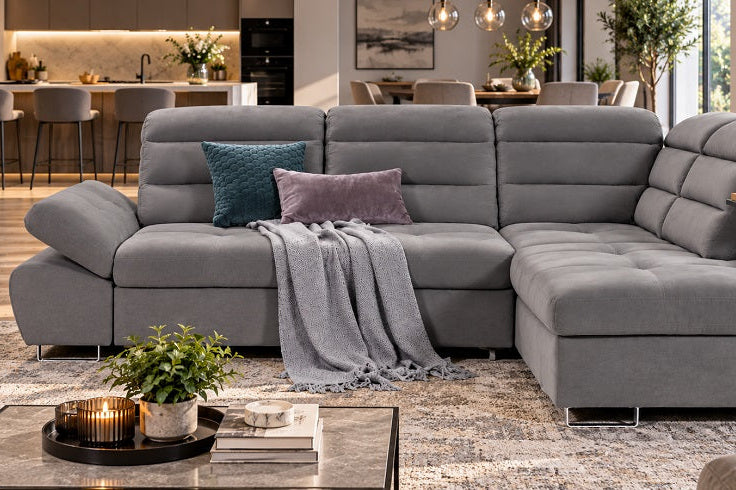 A large gray fabric sectional sofa with a chaise lounge, styled in a modern living room with accent pillows, a throw blanket, and a coffee table in the foreground.