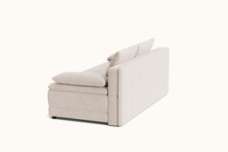 A modern upholstered ottoman or low sofa with a tufted backrest and two loose back cushions, shown from a three-quarters angle on a plain off-white background.