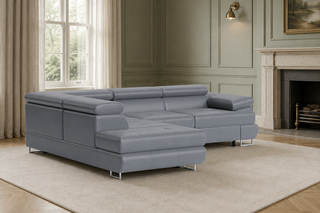 A modern light gray sectional sofa with a chaise lounge, placed on a large cream area rug in a styled living room with wood floors, paneled walls, a window, and a fireplace.